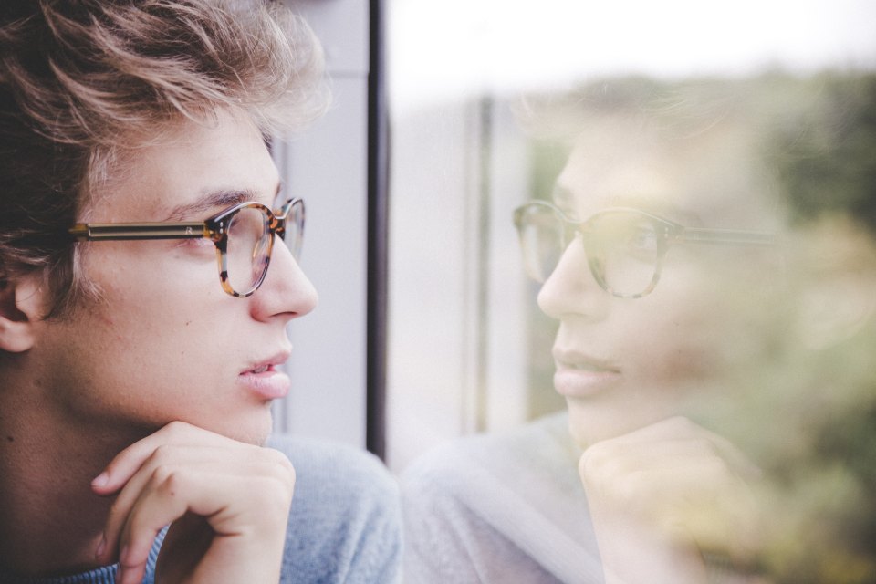 young man looks out a window with his reflection